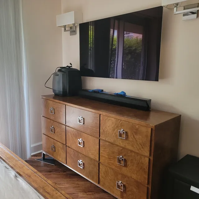 Unit W907 — primary bedroom dresser wall and wall-mounted TV, the terrace doors reflected in the screen