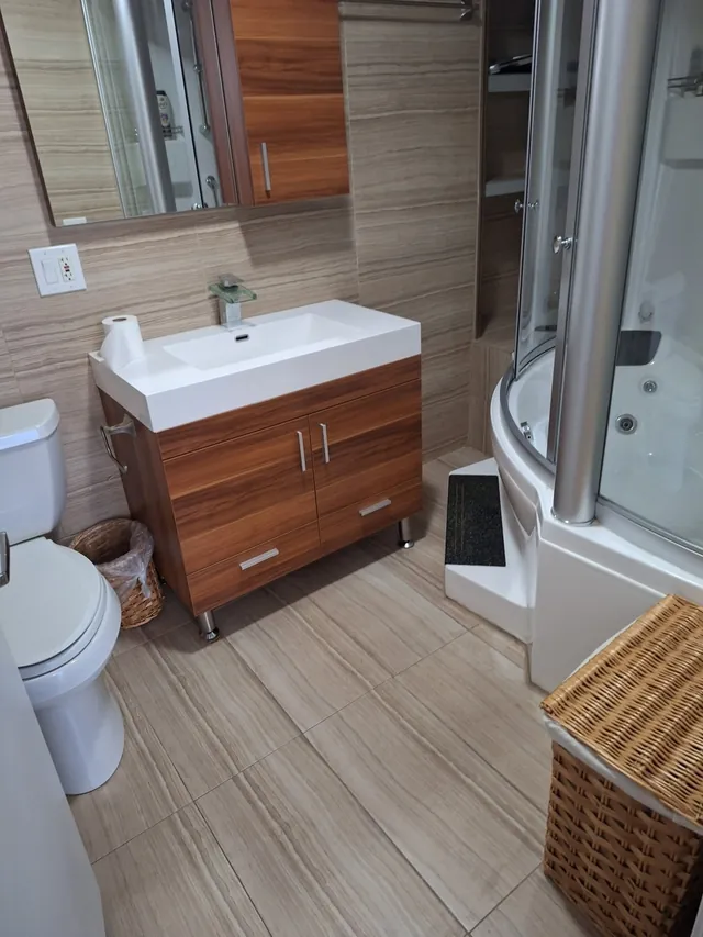 Unit W907 — spa primary bath: marble tile, wood vanity, glass waterfall faucet, and the two-person Jacuzzi with its steam-shower enclosure